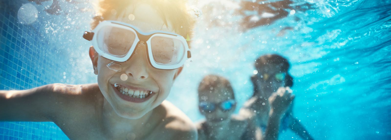 a boy wearing goggles and smiling in a pool