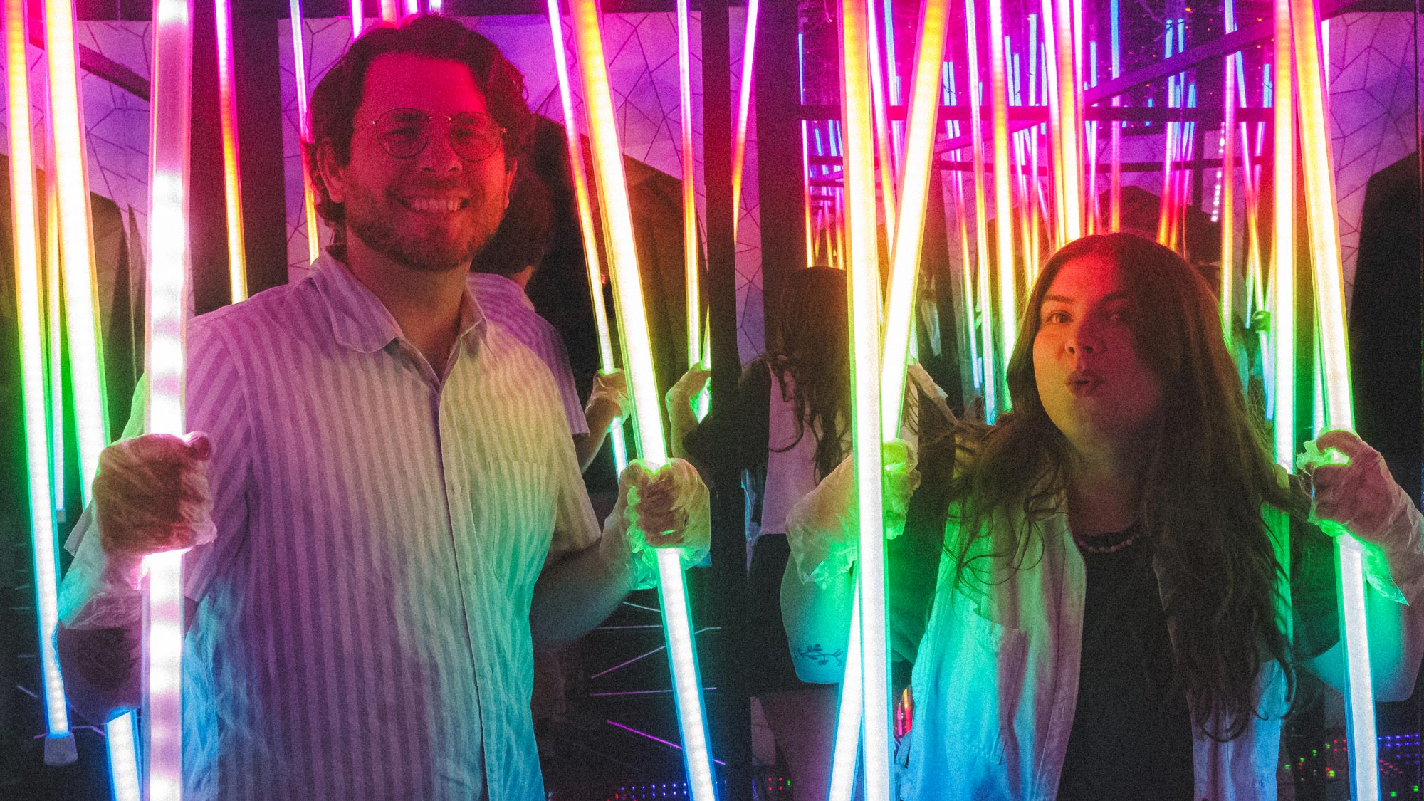 a man and woman in a room with vertical light tubes and a rainbow effect